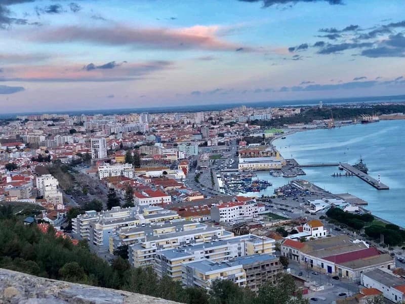 Vista de Setúbal com edifícios residenciais e frente ribeirinha ao fim do dia.